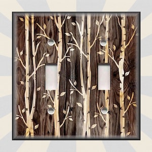 May include: A light switch cover with a wood grain background and a white birch tree design. The switch cover has two toggle switches.
