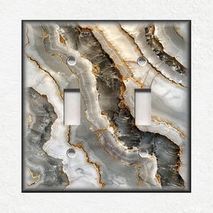 May include: A light switch cover with a marble pattern in shades of gray, white, and gold. The marble pattern has a swirling, abstract design.