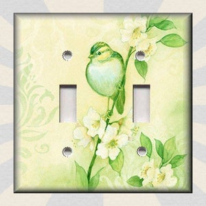May include: A light green and white double light switch cover with a watercolor painting of a green bird perched on a branch with white flowers.