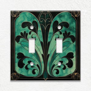 May include: Decorative double light switch cover with an Art Nouveau design. The cover features a teal and black floral pattern with gold accents. The switch plate has two rectangular openings for the switches.