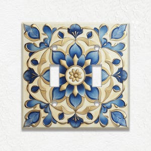 May include: Decorative double light switch cover with a floral design. The cover features a cream-colored background with a blue and gold floral pattern. The design includes stylized flowers and leaves.