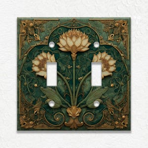 May include: Decorative double light switch cover with a floral design. The cover features a dark teal background with gold and cream-colored floral accents. The design includes two switch openings and four screw holes.