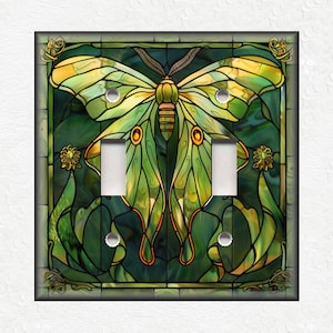 May include: A green and yellow stained glass light switch cover featuring a butterfly with intricate details. The butterfly is surrounded by green and brown foliage.
