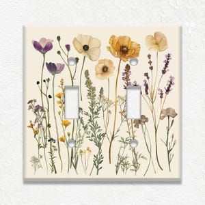 May include: A decorative light switch cover featuring a floral design. The cover has a cream-colored background with watercolor-style illustrations of various flowers in shades of purple, yellow, and orange. The cover has two switch openings and silver screws.