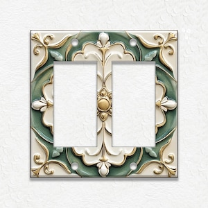 May include: Decorative double light switch cover with a floral design. The cover features a square shape with a cream-colored background, accented with gold and teal green floral patterns. The center has two rectangular openings.