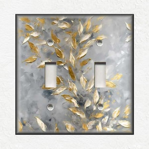 May include: A double light switch cover with a gray and gold abstract design featuring stylized leaves. The design has a painterly look with a textured effect.