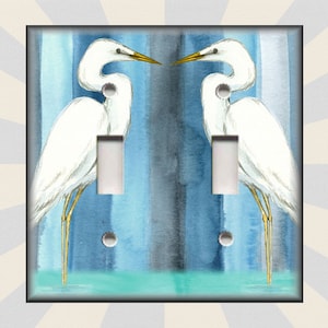 May include: A pair of white egret birds with yellow legs and beaks are standing in blue water with a blue and white striped background. The image is for a light switch cover.