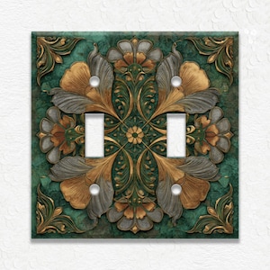 May include: Decorative double light switch cover with a floral design. The cover features a teal green background with gold, gray, and brown floral elements. The design includes two light switch openings and a square shape.