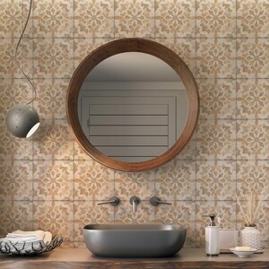 May include: A bathroom vanity with a round wooden framed mirror, a gray ceramic sink, and a brown wooden countertop. The wall behind the sink is tiled with beige and white patterned tiles.