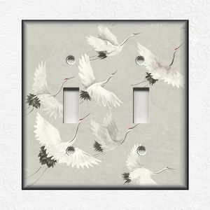 May include: A light gray double light switch cover with a design of white cranes flying in a gray sky.