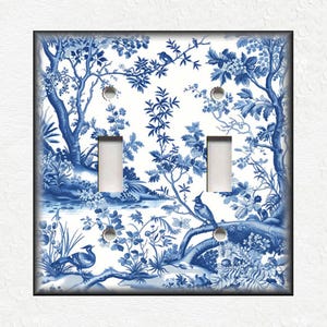 May include: A double light switch cover with a blue and white toile design. The cover features a scenic landscape with birds, trees, and foliage. The design is reminiscent of classic porcelain patterns, adding a touch of elegance to any room.