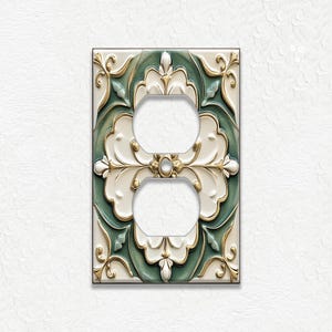 May include: Decorative double electrical outlet cover with a floral design. The cover features a cream-colored background with a green and gold floral pattern. The outlet holes are white.