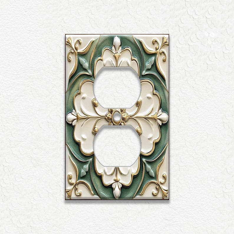 May include: Decorative double electrical outlet cover with a floral design. The cover features a cream-colored background with a green and gold floral pattern. The outlet holes are white.