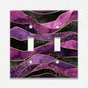 May include: A decorative double light switch cover with a watercolor design. The design features flowing waves of purple, black, and gold. The cover has two switch openings and two screw holes.