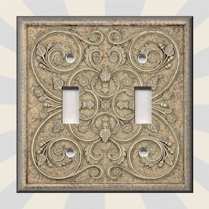 May include: A decorative light switch cover with a beige and brown ornate design. The cover features a swirling floral pattern with a central motif.