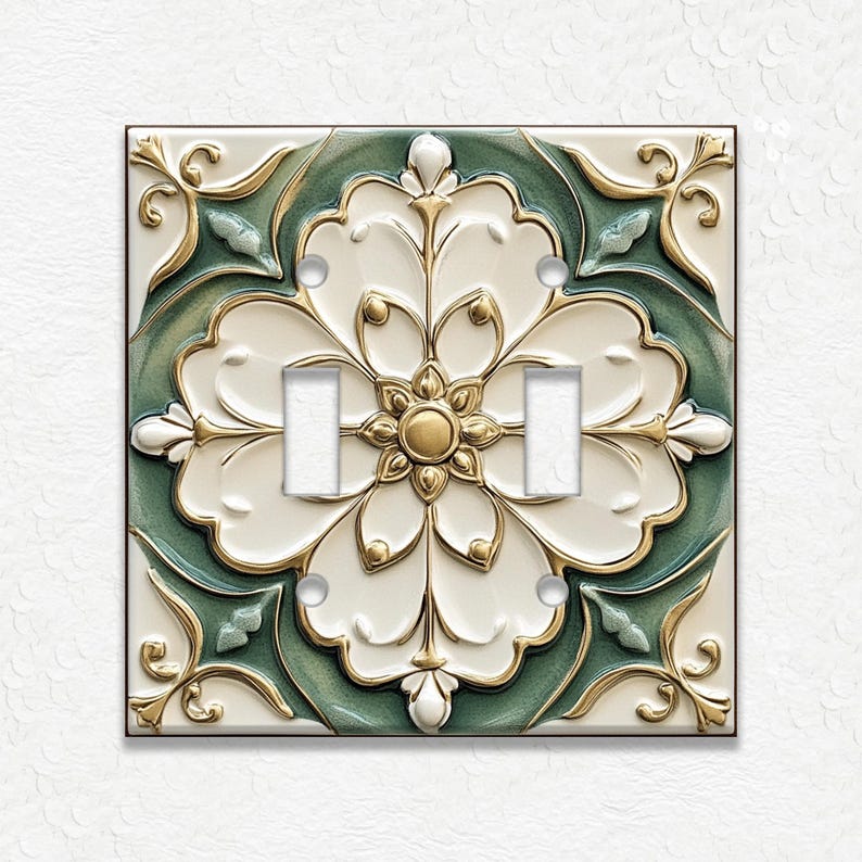 May include: A decorative double light switch cover with a floral design. The cover features a white, green, and gold color scheme. The floral design is centered on the cover and has a raised, three-dimensional appearance.