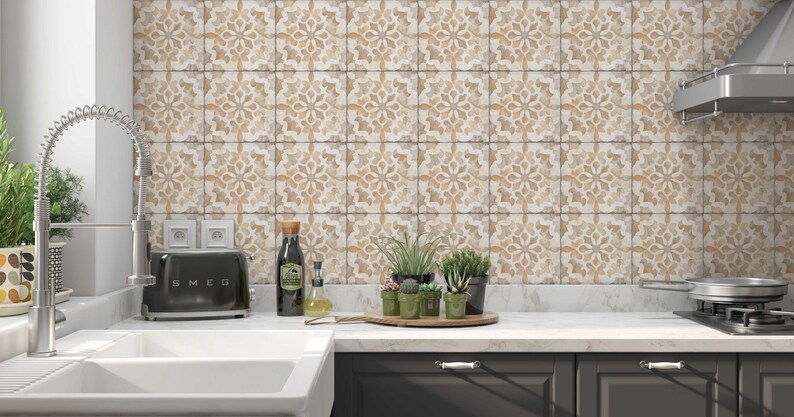 May include: A kitchen with white countertops and gray cabinets. The backsplash is made of beige and brown patterned tiles. There is a stainless steel range hood, a toaster, a sink, and a faucet. There are also plants in pots on the counter.