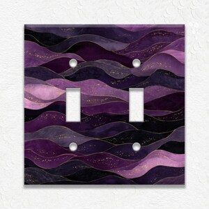 May include: A double light switch cover with a watercolor design of purple and black waves with gold flecks. The cover has two light switch openings and two silver screws.