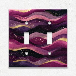 May include: A decorative double light switch cover with a flowing, abstract design. The cover features layers of purple, pink, and gold wavy lines with a speckled pattern. The switch plate has two switch openings and two screw holes.