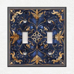 May include: A decorative light switch cover with a blue and gold floral pattern. The design features intricate swirls and leaves.