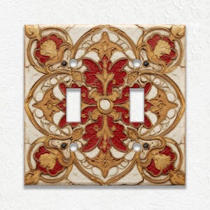 May include: Decorative double light switch cover with a detailed floral design. The cover features a cream-colored background with a red and gold floral pattern. The design is symmetrical and ornate, adding a touch of elegance.