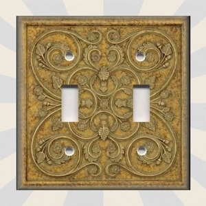 May include: A double light switch cover with an ornate gold and brown design featuring intricate floral patterns.