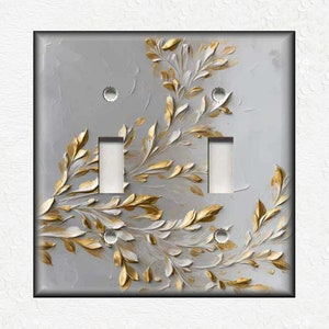May include: A light gray double light switch cover with a decorative design of gold and white leaves.