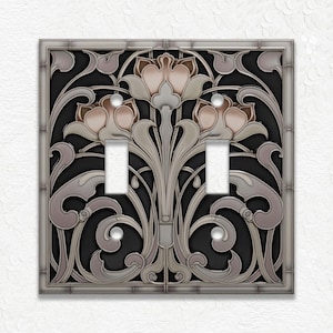 May include: A decorative double light switch cover with an Art Nouveau design. The cover features a black background with a floral pattern in shades of gray, silver, and blush pink. The switch plate has a silver frame and two toggle switch openings.
