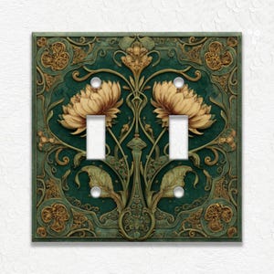 May include: Decorative double light switch cover with a floral design. The cover features a dark teal background with gold and tan floral accents. The design includes two tan flowers and intricate leaf patterns.
