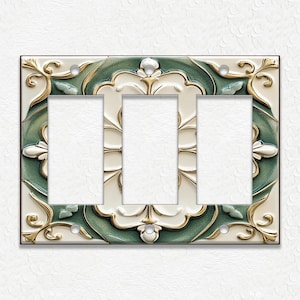 May include: Decorative triple light switch plate with a cream background and a detailed design. The plate features a green and gold floral pattern around the three switch openings. The design has a raised, textured appearance.