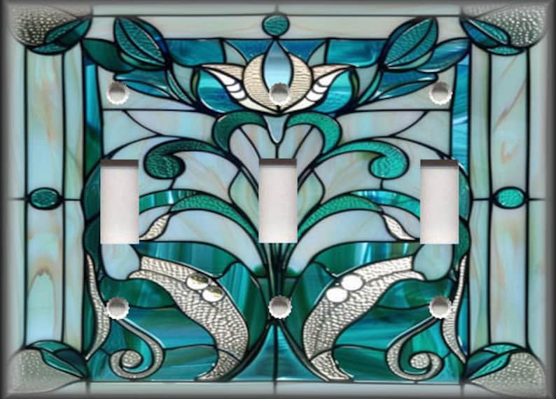 May include: A decorative light switch cover with a stained glass design. The design features teal, white, and silver floral and leaf patterns. The cover has three light switches and a dark border.