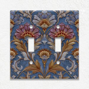 May include: A decorative double light switch cover with a floral design. The cover features a blue background with detailed illustrations of flowers in shades of pink, gold, and cream. The switch openings are white.