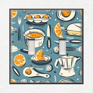 May include: A light blue light switch cover with a colorful pattern of kitchen items, including oranges, a coffee pot, a frying pan, and a pot.