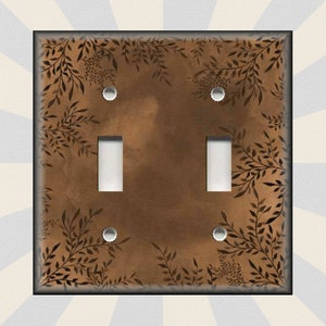 May include: A brown light switch cover with a black leafy pattern. The switch cover has two toggle switches and two screw holes.