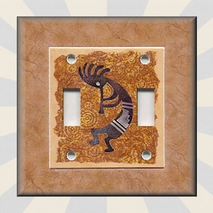 May include: A light brown switch plate with a decorative design featuring a stylized Native American dancer in black and white. The dancer is holding a flute and is surrounded by a brown and gold patterned background.