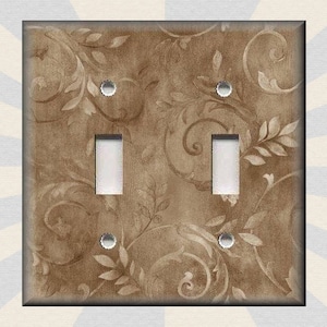 May include: A light brown double light switch cover with a decorative floral pattern. The switch cover has two toggle switches and two screw holes.