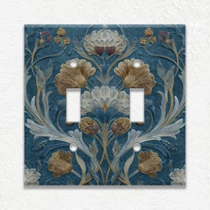 May include: A decorative double light switch cover with a floral design. The cover features a blue background with a repeating pattern of stylized flowers in shades of gold, white, and blue. The switch openings are white.