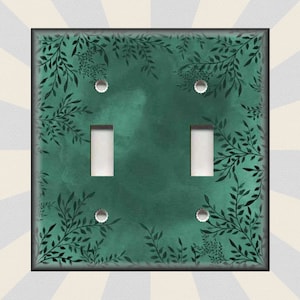 May include: A green light switch cover with a black leafy pattern. The switch cover has two toggle switches.