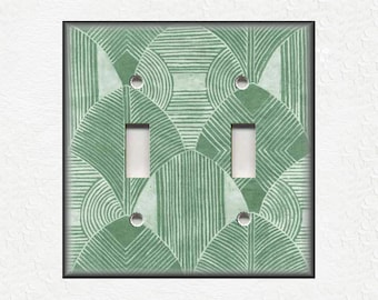 Puede incluir: Una placa de interruptor doble de color verde claro con un patrón geométrico de círculos y líneas superpuestos.