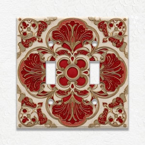 May include: Decorative double light switch cover with a floral design. The cover features a cream background with a red and gold floral pattern. The design is symmetrical, with a central flower and four corner accents.