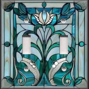 May include: A decorative light switch cover with a stained glass design. The cover features a floral pattern in shades of teal, white, and silver. The design includes two light switch openings and silver-colored screws.