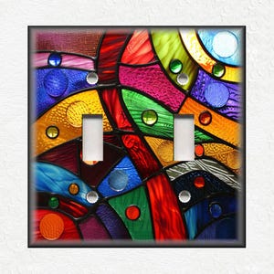May include: A colorful stained glass design with red, yellow, blue, green, and purple hues. The design features geometric shapes and circles. The design is on a light switch plate.