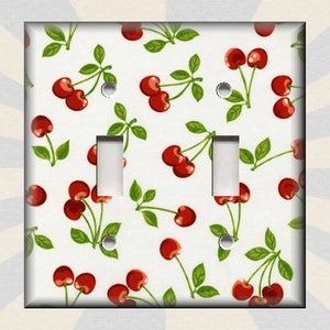 May include: A white light switch cover with a red cherry pattern. The cherries are on stems with green leaves.