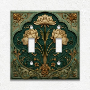 May include: Decorative double light switch cover with a floral design. The cover features a dark teal background with gold and cream-colored floral accents. The design includes two light switch openings and two screw holes.