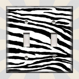 May include: A black and white zebra print light switch cover. The cover has two toggle switches.