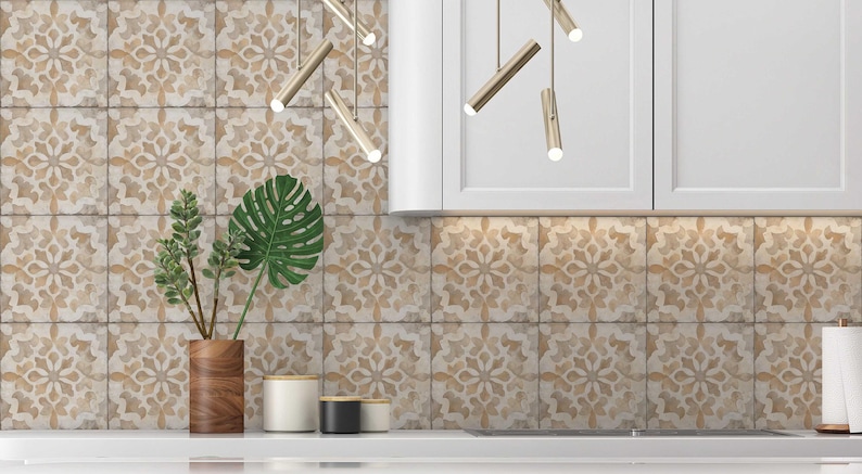 May include: A kitchen backsplash with beige and brown patterned tiles. The tiles have a floral design. There are two plants in wooden pots and three decorative containers on the counter.