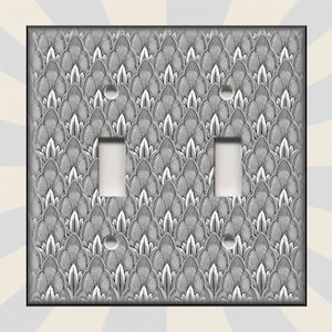 May include: A light switch cover with a black and white geometric pattern. The pattern resembles overlapping scales or leaves.