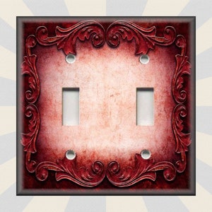 May include: A double light switch cover with a red and white distressed background. The cover has a decorative ornate border in a dark red color.