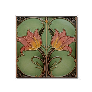 May include: A green ceramic tile with a decorative design of two stylized flowers with orange and pink petals. The flowers are surrounded by a copper-colored floral pattern.