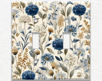 May include: A decorative double light switch cover featuring a floral pattern. The design includes blue, white, and tan flowers and foliage on a cream background. The cover has two switch openings and screw holes.